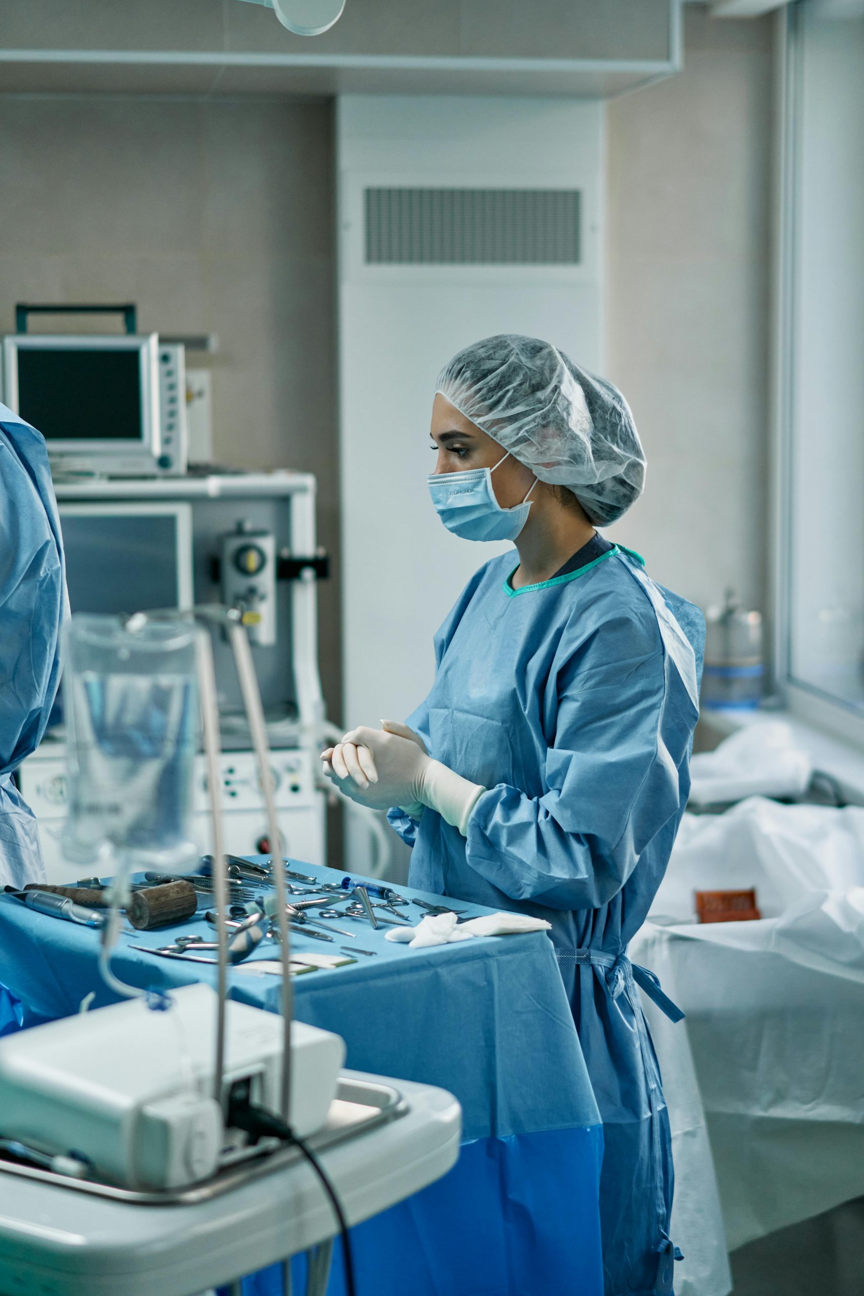 Surgeon wearing personal protective equipment arranging medical tools in a sterile operating room.