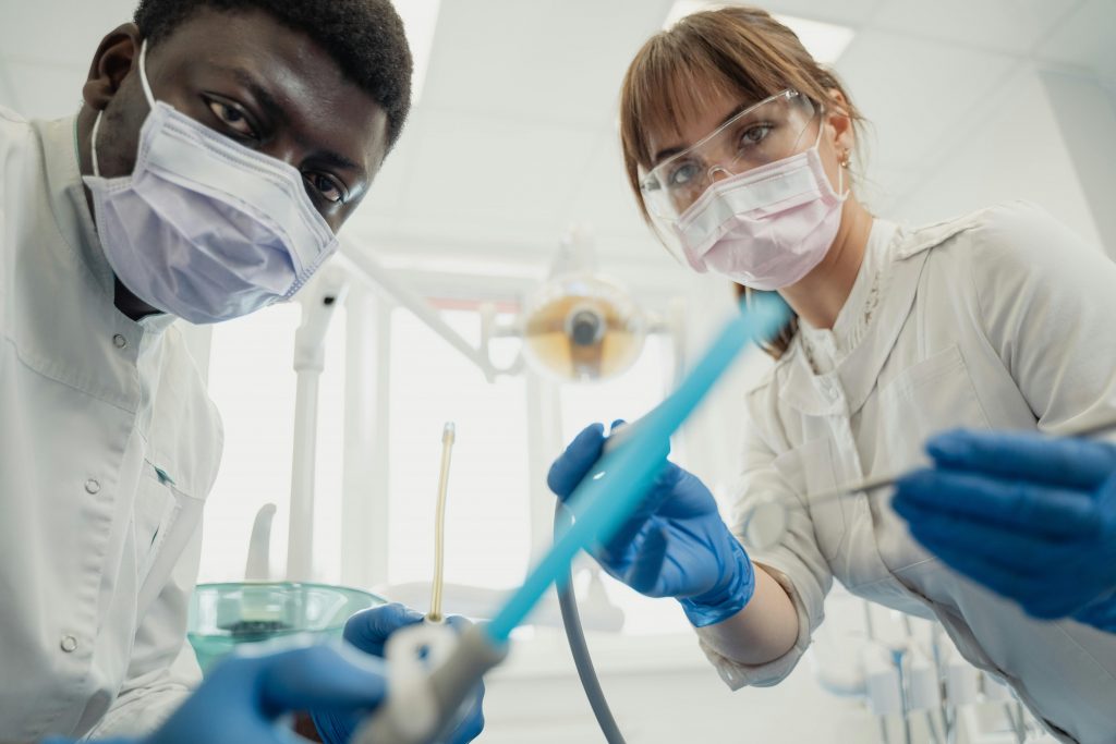 Two dentists in protective gear examining a patient with dental tools in a clinic.