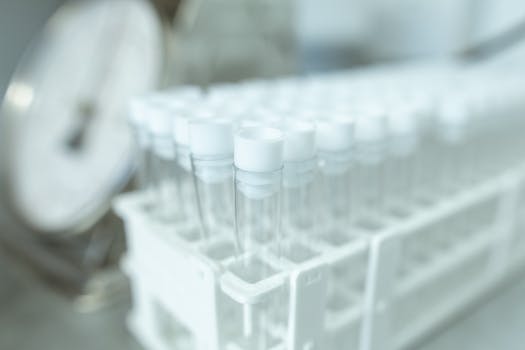Rows of transparent test tubes in a rack, set in a laboratory environment with medical equipment.